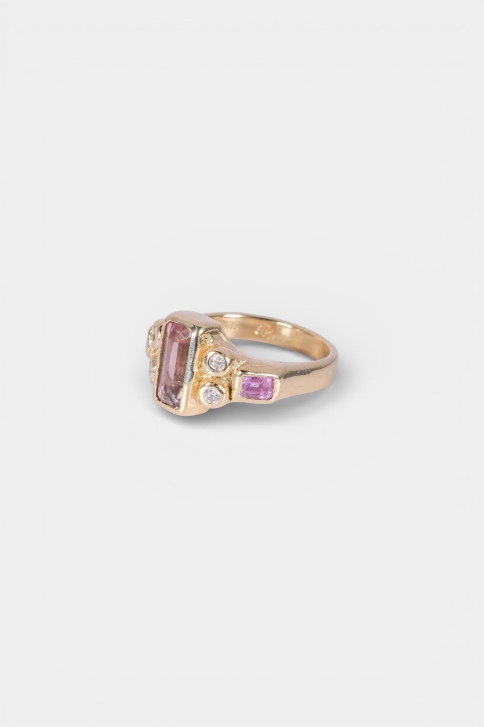Gold ring with pink gemstones on a light gray background